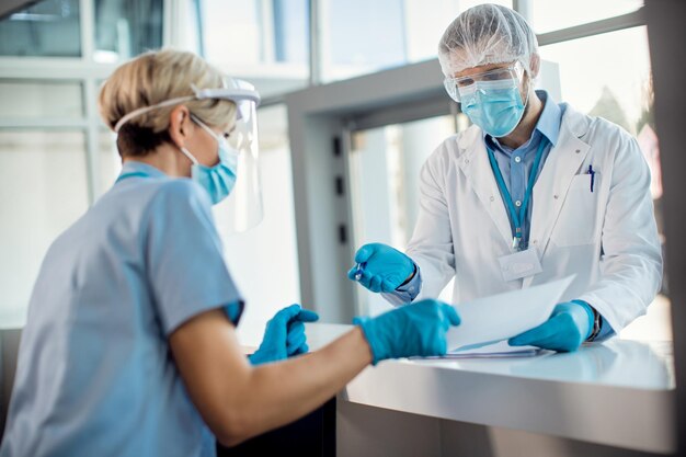 Doctor in protective workwear cooperating with a nurse at reception desk in the hospital