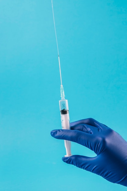 Doctor's hand with injection on blue backdrop