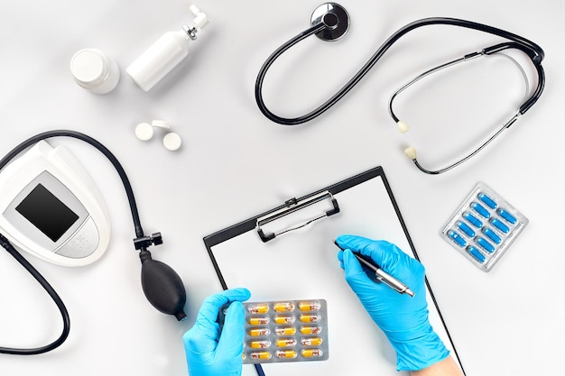 의사의 탁자, 도구, 의료 기기, 치료사 안압계, 혈압, 흰색 바탕에 평평한 위치에 있는 병원에서 일합니다. 파란색 장갑을 낀 의사의 손은 흰색 종이에 표시기를 기록합니다