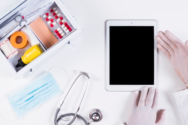 Doctor showing blank screen on digital tablet with medical equipments on white backdrop