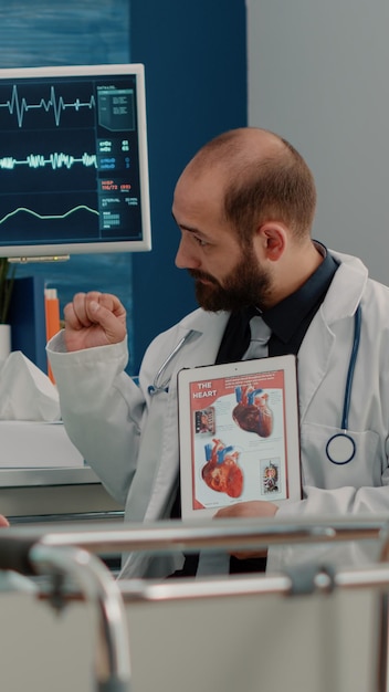 Doctor showing cardiovascular image on tablet to ill patient in hospital bed. Senior woman with sickness looking at cardiology figure with blood vessel on display for diagnosis.