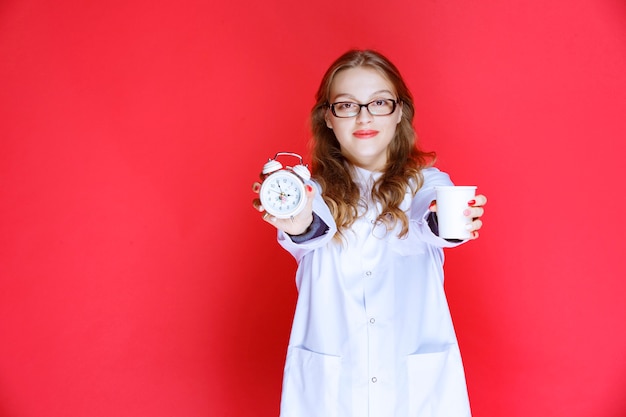 Medico che mostra l'orologio e la tazza dell'acqua che significano prendere le medicine in tempo.