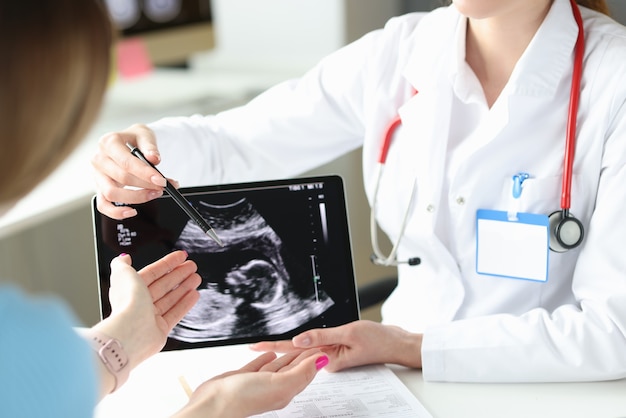 Doctor showing patient woman ultrasound scan of fetus on digital tablet closeup