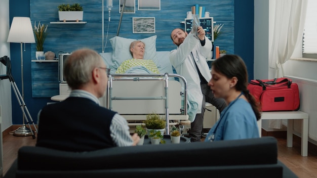 Доктор показывает рентген пожилой женщине, лежащей на больничной койке. Медик объясняет рентгенографию пенсионеру с болезнью для диагностики и лечения. Больной пожилой человек с проблемами со здоровьем