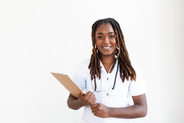 Doctor smiles while staring out window in hospital hallway and holding clipboard with patient file