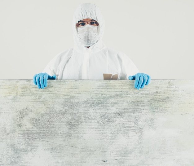 Foto gratuita un medico in piedi in bianco e tavola di legno in maschera, guanti e tuta protettiva