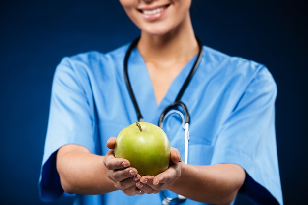 Doctor swith stethoscope holding and showing green apple