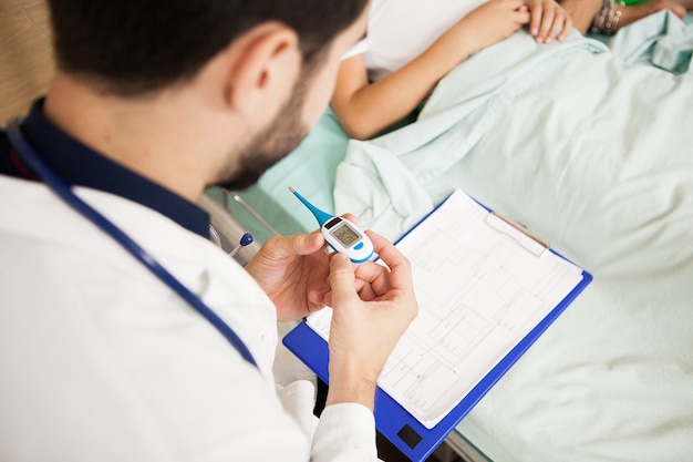 Foto gratuita medico che misura la temperatura corporea del suo paziente nella stanza d'ospedale