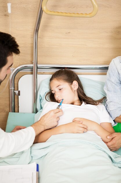 Doctor taking body temperature of her patient in hospital room