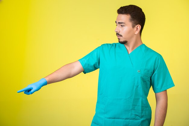 Doctor in uniform and hand mask showing something aside.