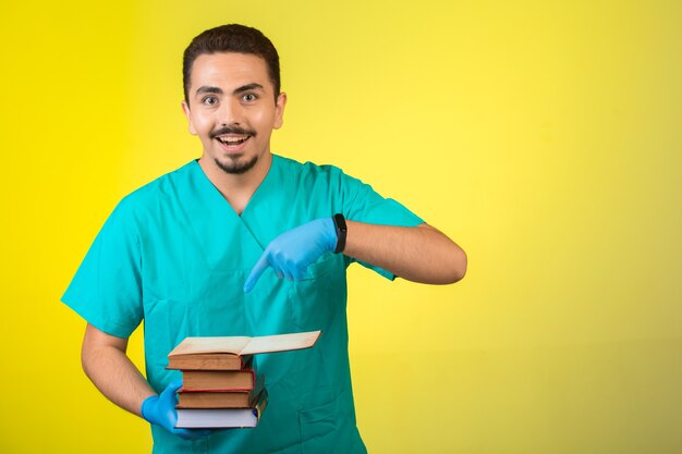 Doctor in uniform and hand mask standing and pointing his books meaning his education.