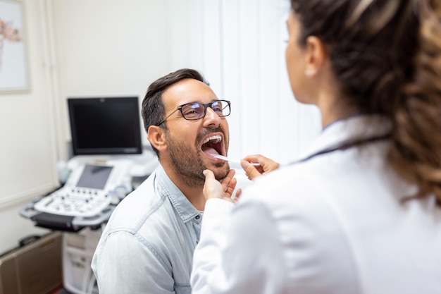 Doctor using inspection spatula to examine patient throat ENT doctor doing throat exam patient opened his mouth to throat checkup