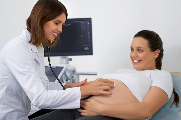 妊娠中の女性を検査するために聴診器を使用している医師