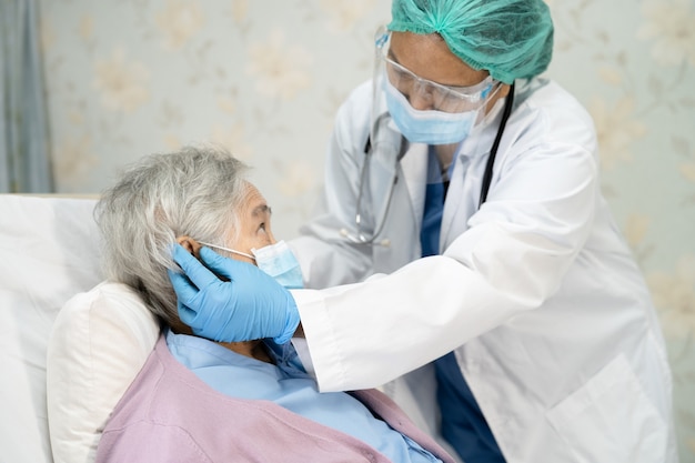 聴診器​を​使用して​、​感染​を​防ぐ​ために​病院​で​フェイス​マスク​を​着用している​アジア​の​高齢者​または​高齢​の​老​婦人​女性​患者​を​チェックする​医師​covid​-​19​コロナ​ウイルス​。