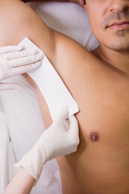 Doctor waxing male patient skin in clinic