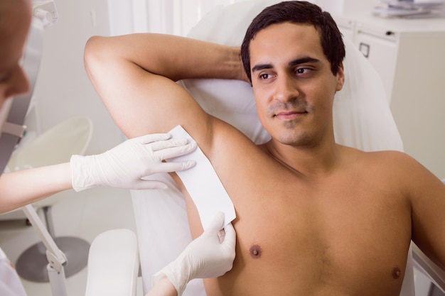 Doctor waxing male patient skin