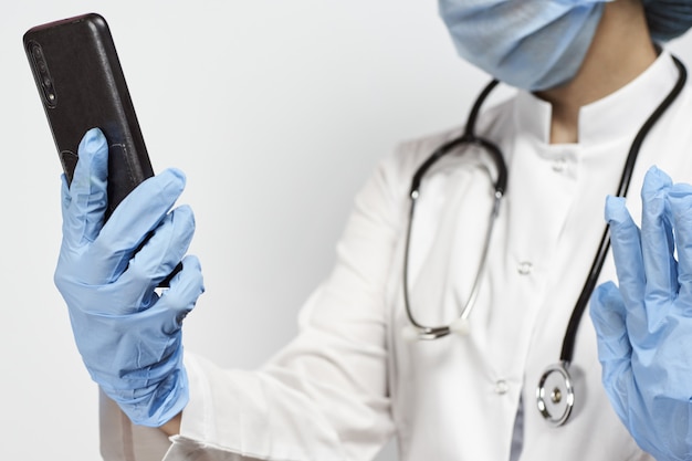 Doctor wearing gloves and a face mask and holding a smartphone