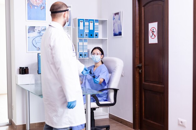 Doctor wearing protective coat and face mask against coronavirus while giving nurse patient radiography in hospital waiting room