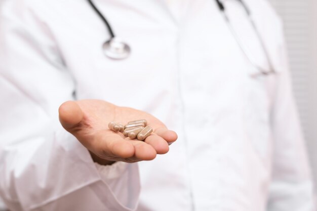 Doctor in a white coat holding pills in a hand.
