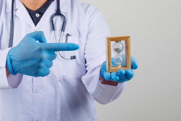 Doctor in white coat showing hourglass in his hand