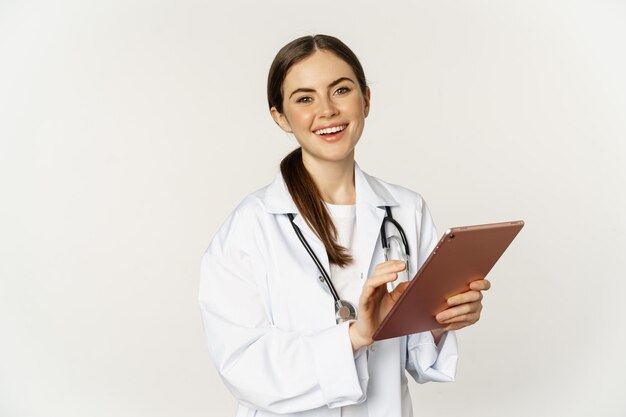 Doctor in white coat using digital tablet reading medical data on gadget working in hospital standin...