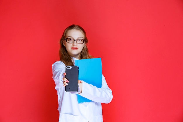 Doctor with a blue folder showing her phone.