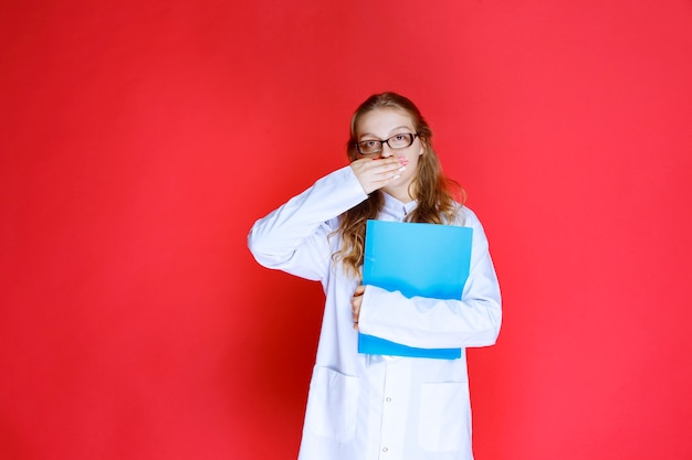 Doctor with eyeglasses holding a blue folder and looks tired.