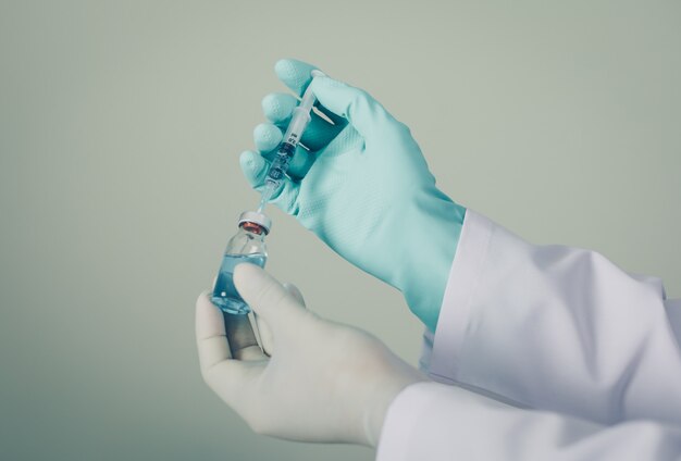 Doctor with gloves drawing medicine out of a vial. side view.