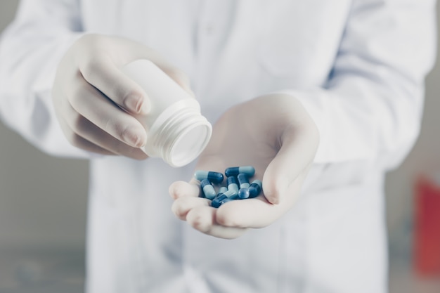 Doctor with gloves holding pills and bottle, side view.