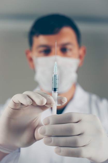 Doctor with gloves holding syringe with his hands, side view.