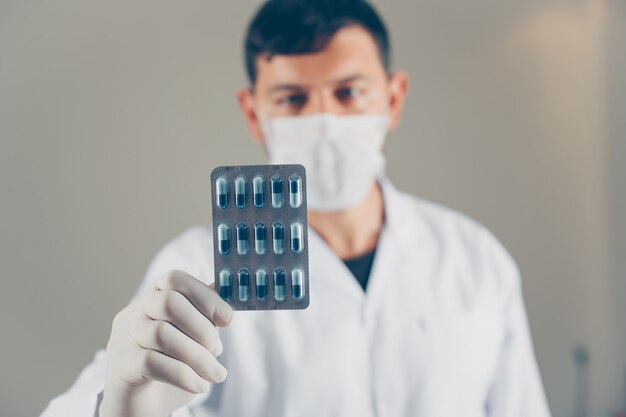 Doctor with gloves and mask holding a pill packet. side view.