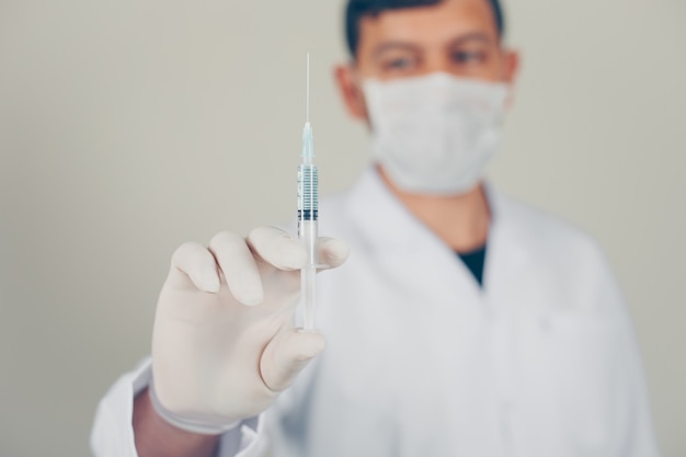 Doctor with gloves and mask holding a syringe. side view.