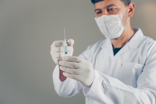 Doctor with gloves and mask holding and tapping on syringe. side view.