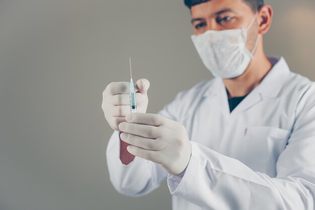 Doctor with gloves and mask holding and tapping on syringe. side view.