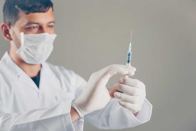 Doctor with gloves and mask looking at syringe and holding syringe with his hands. side view.