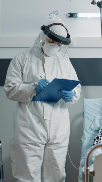 Doctor with hazmat suit doing checkup visit for aged woman having coronavirus symptoms in lockown area. Medic consulting healthcare of ill patient with oxygen mask during pandemic outbreak