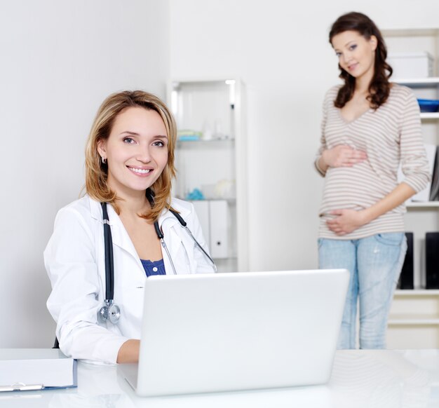 Doctor with laptop and young pregnant woman in hospital - indoors