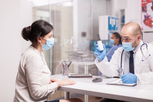 Doctor with mask against coronavirus holding pills bottle for patient.