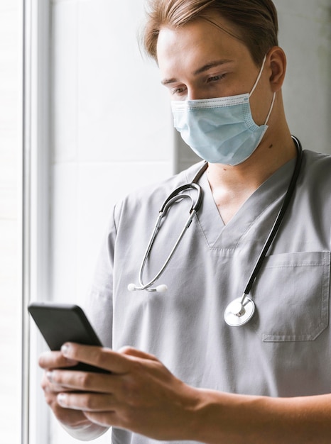 Бесплатное фото Доктор с медицинской маской проверяет смартфон