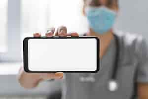 Free photo doctor with medical mask holding smartphone