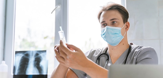 Doctor with medical mask holding syringe