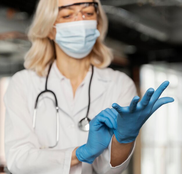 Doctor with medical mask putting on medical gloves
