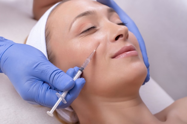 Doctor with rubber gloves doing a plastic face surgery on a happy young female