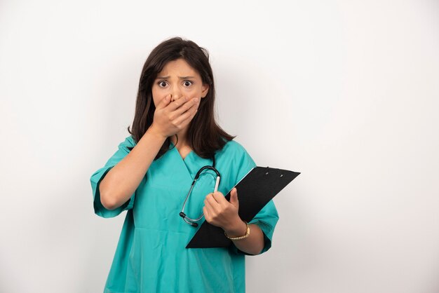 Doctor with stethoscope and clipboard covering her mouth on white background. High quality photo