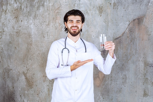 Doctor with a stethoscope holding a glass of pure water and pointing at somewhere