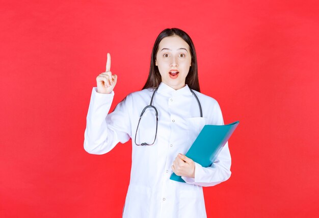 聴診器を持った医師が患者の病歴を保持し、手を挙げて質問します。
