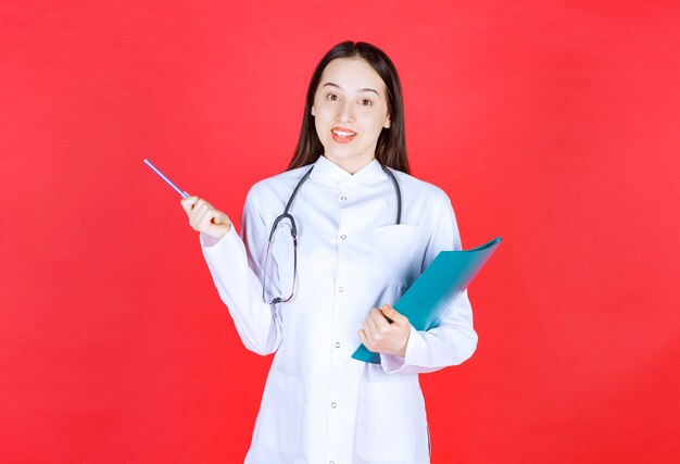 Doctor with a stethoscope holding the history of the patient and raising hand to ask a question.