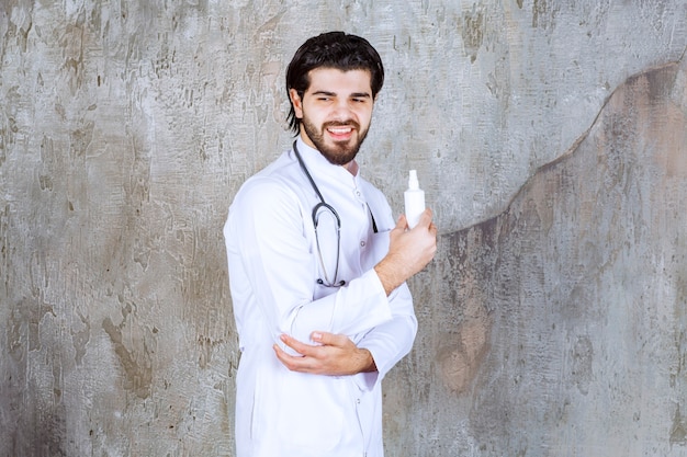 Medico con uno stetoscopio che tiene un tubo bianco di spray disinfettante per le mani