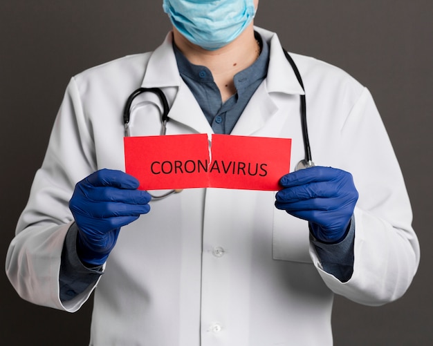 コロナウイルスで破れた紙を保持している手術用手袋を持つ医師