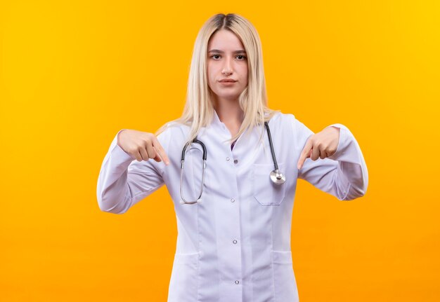 Врач молодая девушка со стетоскопом в медицинском халате указывает вниз на изолированную желтую стену